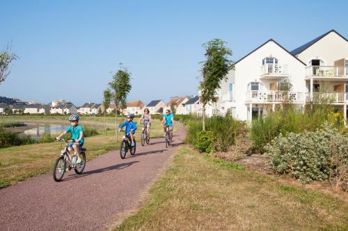 a group of people riding bikes down a road at Pierre & Vacances Résidence Le Chant des Oiseaux in Courseulles-sur-Mer