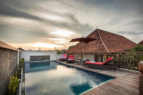 Una piscina con sillas y una sombrilla en una terraza. en Svarna Hotel, en Sanur