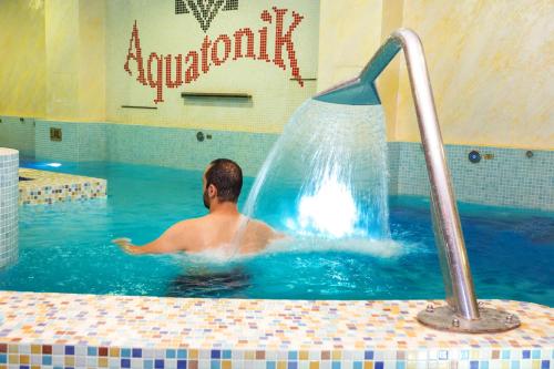 a man in a swimming pool with a water fountain at Balneo Complex & Spa Aquatonik in Velingrad