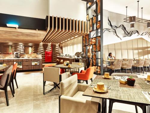 a restaurant with tables and chairs and a kitchen at Novotel Karawang in Karawang