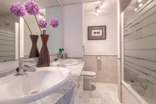 baño con lavabo y 2 jarrones con flores púrpuras en Penthouse Princesa Kristina en Manilva