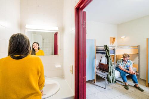 a woman standing in a bathroom looking in a mirror at Auberge de Jeunesse de Namur in Namur