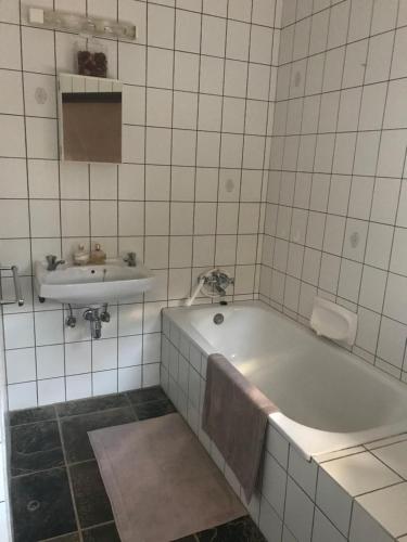 La salle de bains est pourvue de carrelage blanc, d'une baignoire et d'un lavabo. dans l'établissement The Farmhouse, à Okahandja