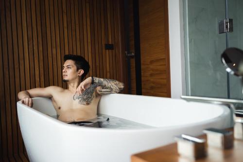 a man with a tattoo sitting in a bath tub at The Gallery Hotel Nai Harn in Nai Harn Beach