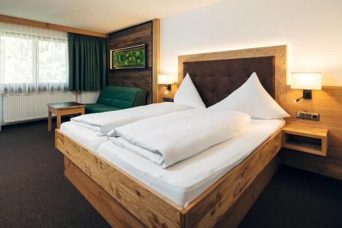 a bedroom with a large bed and a green chair at Hotel Barbara in Serfaus