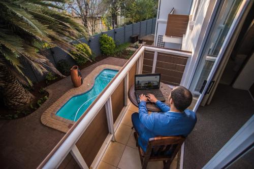 a man sitting in a chair with a laptop next to a swimming pool at Adelante Lodge in Bloemfontein