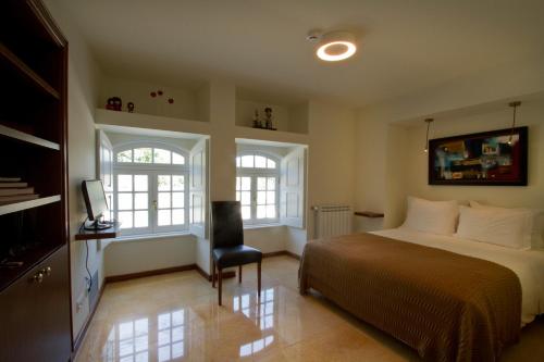 a bedroom with a bed and two windows and a chair at Quinta de Lograssol in Mealhada