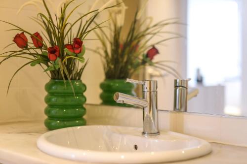a bathroom sink with a green vase with red flowers at Seaside Family Townhouse - 100m from the sea! in Cascais