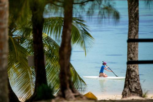 a woman riding a paddle board on the water at Tamanu Beach in Arutanga