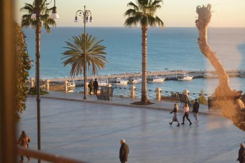 people walking on a sidewalk near the ocean with palm trees at BnB Agorà Panoramic Rooms in Sciacca