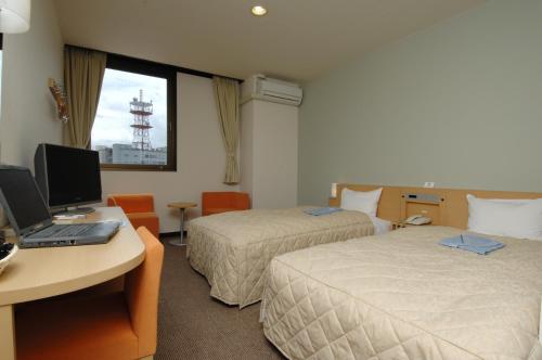 a hotel room with two beds and a desk with a laptop at Hamada New Castle Hotel in Hamada