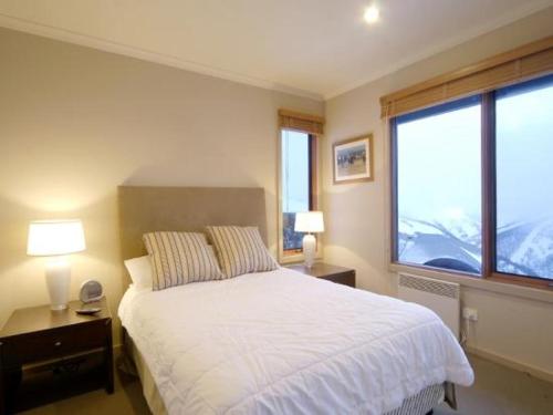 a bedroom with a white bed and two windows at Ultima Apartments in Mount Hotham