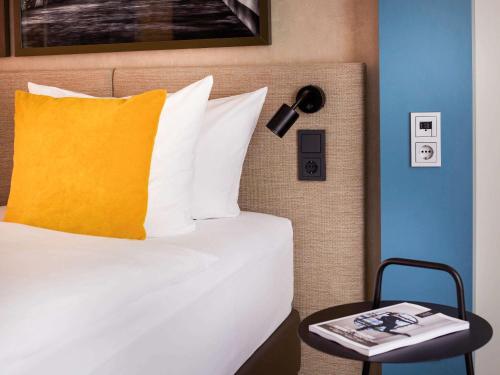 a bed with a yellow pillow and a side table at Hotel Mondial am Dom Cologne MGallery in Cologne