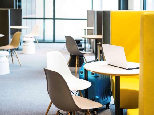 a room with tables and chairs with a laptop on a table at Ibis Schiphol Amsterdam Airport in Badhoevedorp