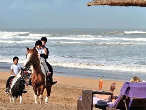two people riding a horse on the beach at Pullman Mazagan Royal Golf & Spa in El Jadida