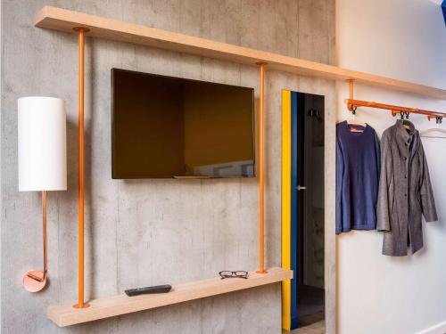 a flat screen tv on a wall with a shelf at ibis budget Metz Technopole in Metz
