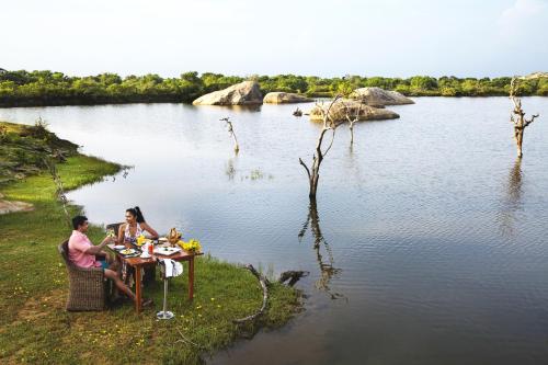 a man and woman sitting at a table by a lake at Cinnamon Wild Yala in Yala