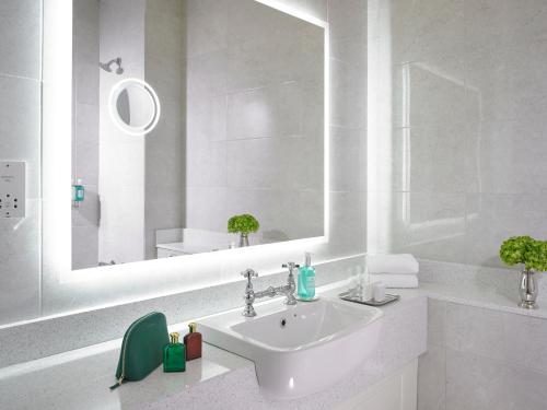 ein weißes Badezimmer mit einem Waschbecken und einem Spiegel in der Unterkunft Fitzgeralds Woodlands House Hotel in Adare