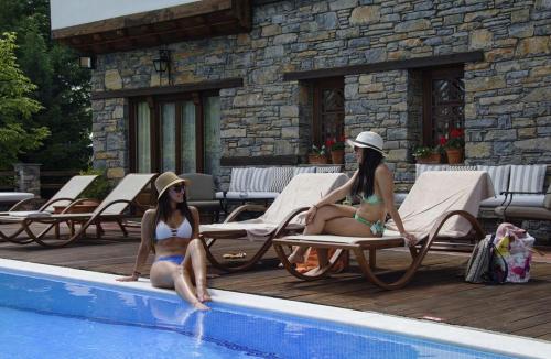 two women in bathing suits sitting next to a swimming pool at Archontiko Naoumidi in Portariá