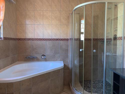La salle de bains est pourvue d'une baignoire et d'une douche en verre. dans l'établissement Malu Guest House, à Witbank