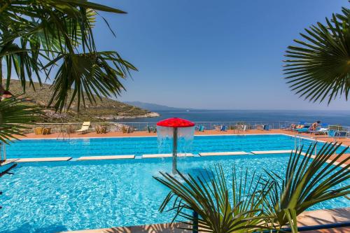 ein Pool mit einem roten Regenschirm und dem Meer in der Unterkunft Hotel Bahamas in Sarandë