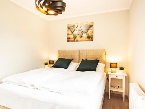 a white bedroom with a large white bed and a chandelier at VacationClub – Rezydencja Park Orła Apartament 12 in Mielno