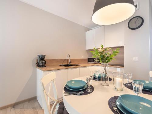 a white kitchen with a table and chairs and a clock at VacationClub – Rezydencja Park Orła Apartament 12 in Mielno