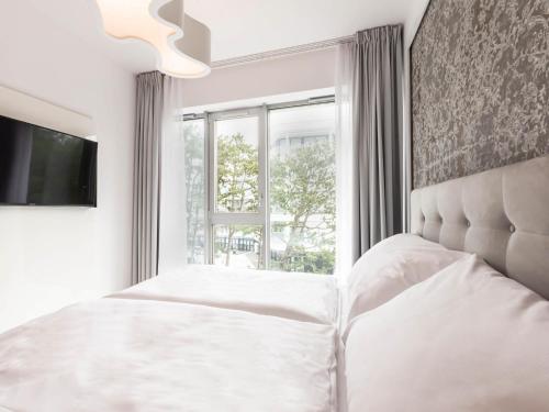 a white bedroom with a bed and a window at VacationClub – Dune B Apartament 3.22 in Mielno