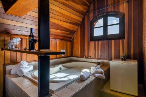 a bathroom with a tub with a bottle of wine and towels at Pousada Cantos e Contos in Monte Verde