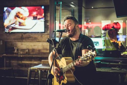 un homme jouant de la guitare devant un microphone dans l'établissement St Christopher's Inn Shepherd's Bush, à Londres