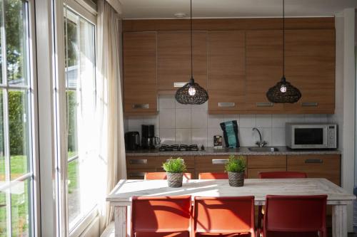 a kitchen with a table with orange chairs and a kitchen with a window at Bunckman 10 pers. bungalow in Voorthuizen