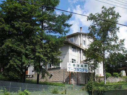 a white building with a sign in front of it at Kusatsu Kogen Youth Hostel in Kusatsu