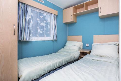 2 camas en una habitación con paredes azules y ventana en MB Beach Cottage, en Hoek