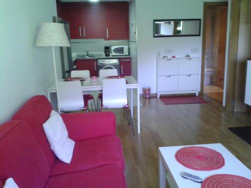 a living room with a red couch and a kitchen at TORRE de la FUENTE AprtoVistas Piscina Parking in Oviedo