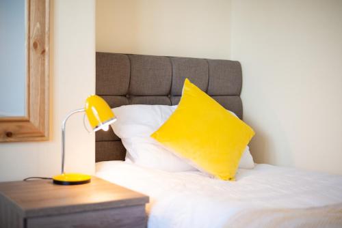 a bed with a yellow pillow and a lamp on a table at Off Road parking, Garden, TV in Every Room in Swansea