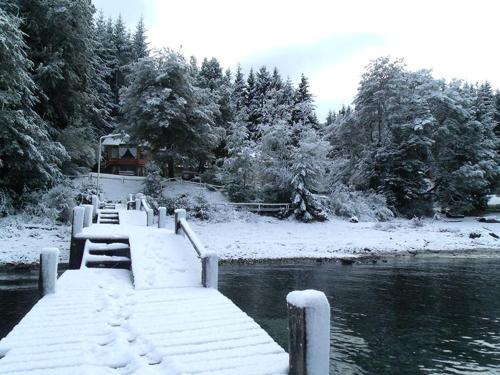 a snowy dock with a house in the middle of a river at Cabañas Rincon del Lago in Villa La Angostura