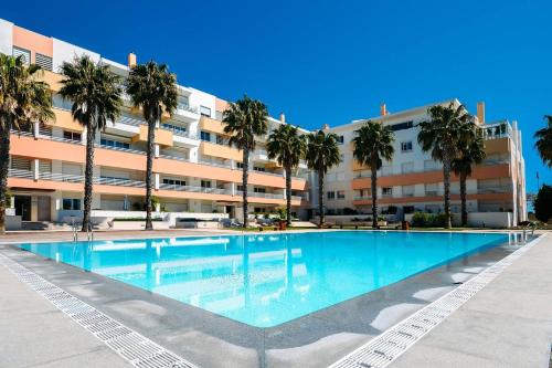a large swimming pool with palm trees in front of a building at Fantastic Seaside Family Apartment with Pool in Parede