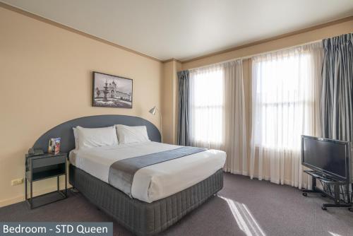 Clocktower Apartment Hotel في ملبورن: غرفة فندقية بسرير وتلفزيون بشاشة مسطحة