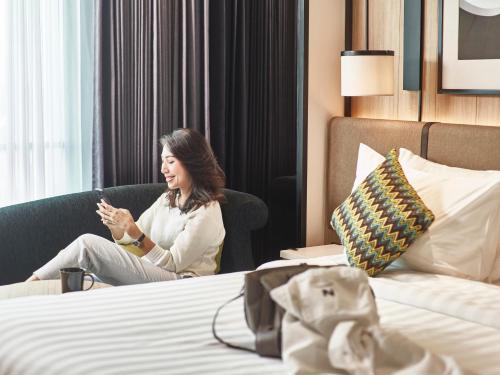 a woman sitting in a chair in a hotel room at Novotel Karawang in Karawang