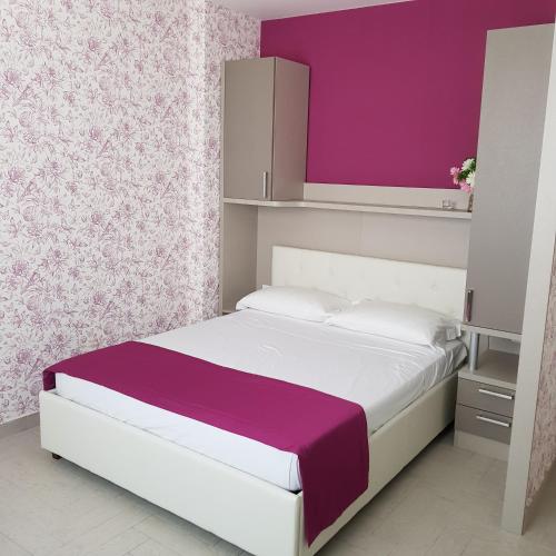 - une chambre avec un lit blanc et un mur violet dans l'établissement Eden Room, à Margherita di Savoia
