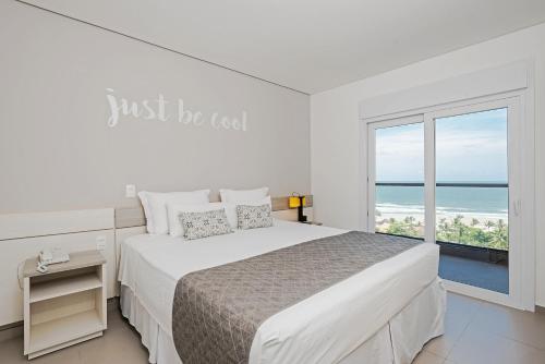 a white bedroom with a bed and a large window at Guarujá Vivah in Guarujá