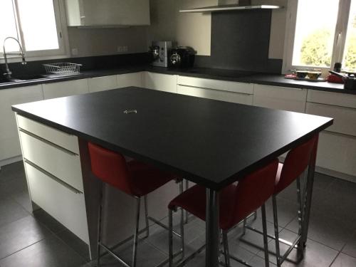 una isla negra en una cocina con dos sillas rojas en Grande chambre chez l habitant, sanitaires partagés avec éventuels autres locataires, en Buros
