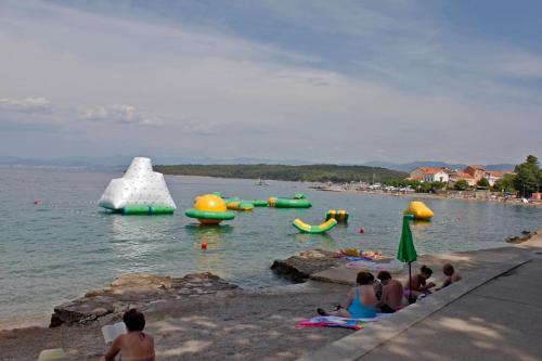 a group of people sitting on the beach near the water at Apartments Matic in Njivice