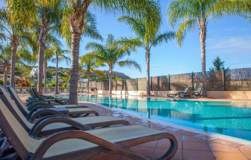 a row of lounge chairs next to a swimming pool with palm trees at B27 - LuzBay 2 Bed Apartment in Luz