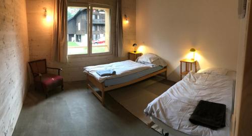 Zimmer mit 2 Betten, einem Fenster und einem Stuhl in der Unterkunft Chalet Vicky et Nino in Les Diablerets
