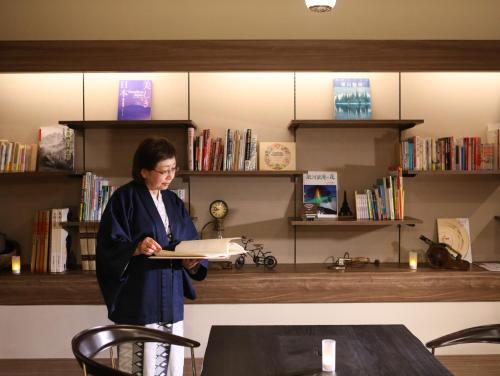 una mujer parada en una biblioteca sosteniendo un libro en Besshoonsen Nanjyo Ryokan, en Ueda