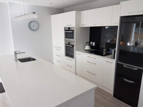 una cocina con armarios blancos y un reloj en la pared en Delightful Petone Townhouse en Lower Hutt