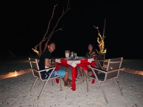two people sitting at a table on the beach at night at Hudhuvelimaldives in Omadhoo