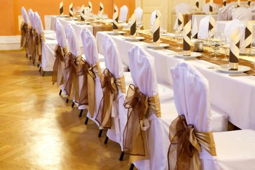 a row of tables with white chairs with bows at Arany Bárány Hotel in Zalaegerszeg