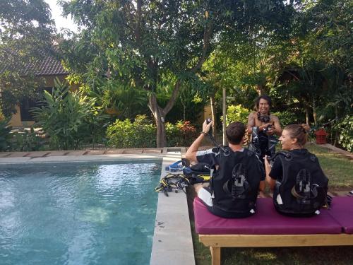a group of people sitting on a bench by a pool at Mango Moon in Pemuteran